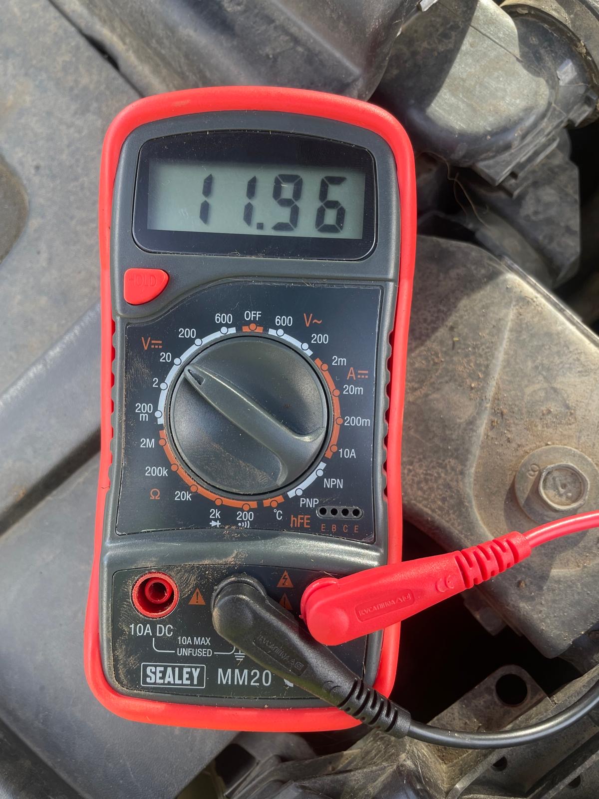 Multimeter reading 11.96V on a flat tractor battery — well below the 12.6V minimum for a healthy charge