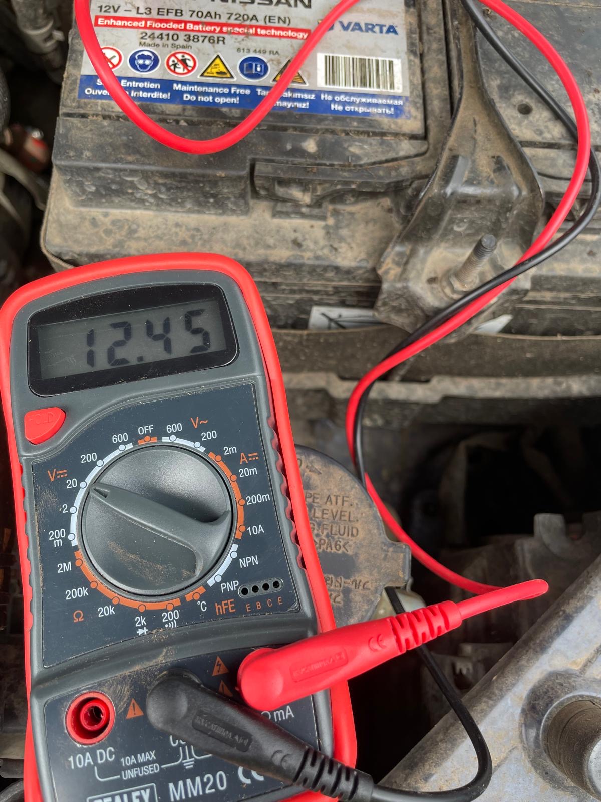 Multimeter reading 12.45V on a tractor battery — a healthy resting voltage indicating a good charge